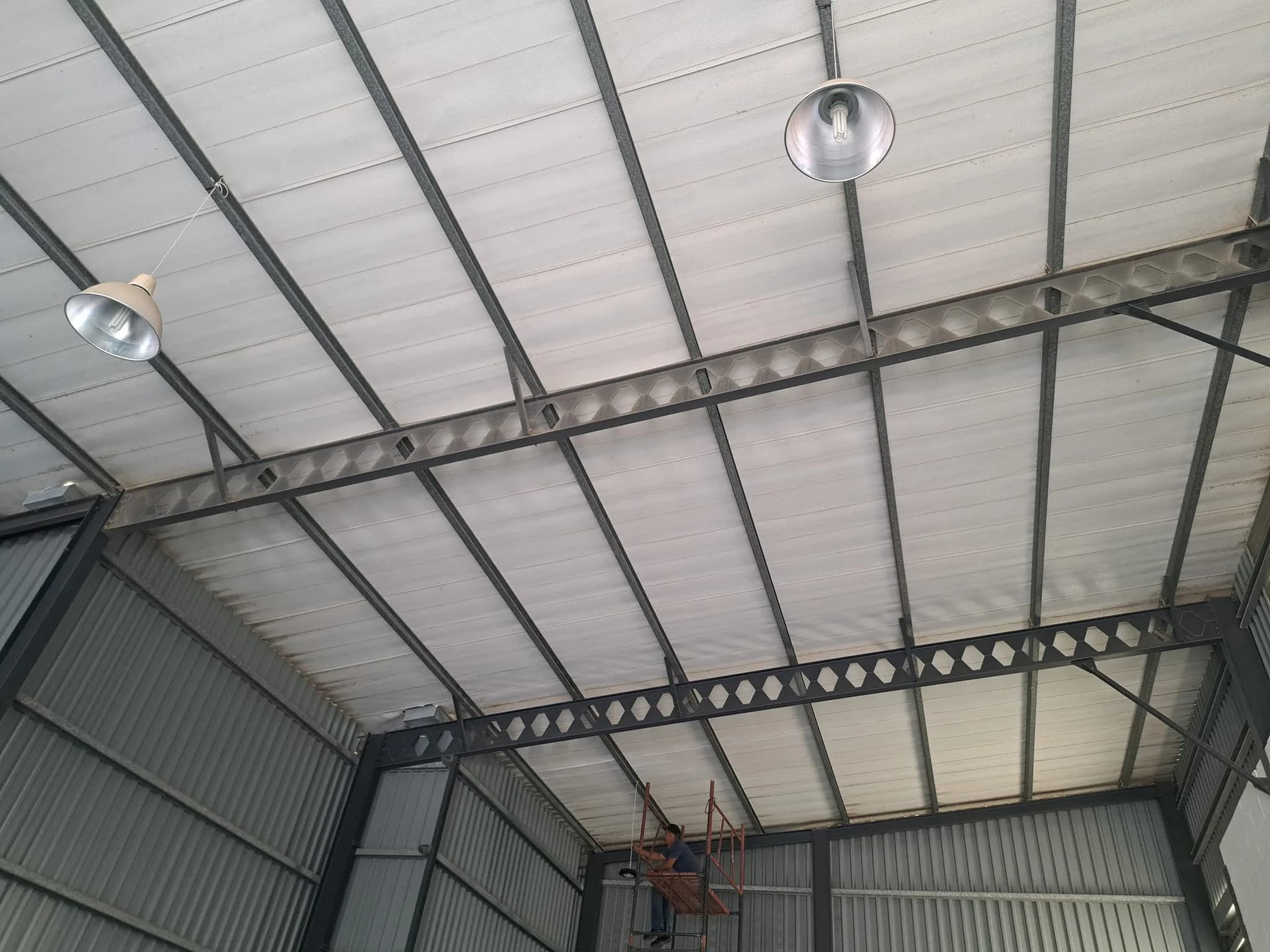 Electrician installing lighting in a warehouse roof structure